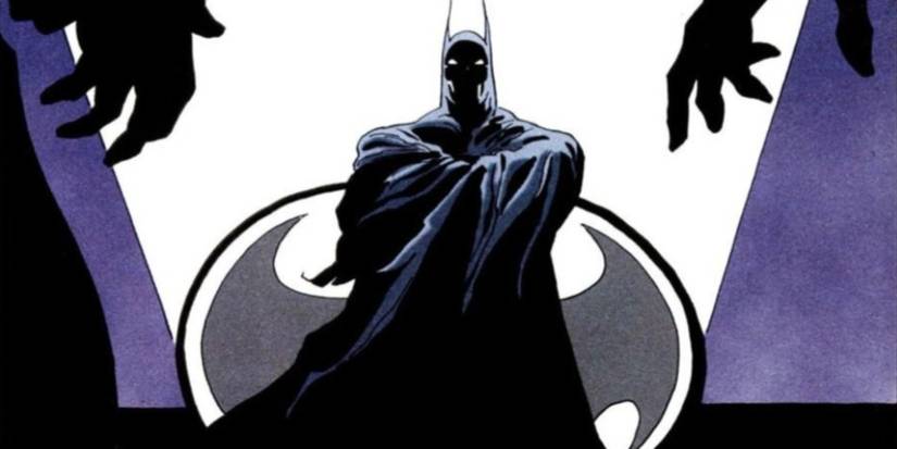 Batman is draped in his cape and standing in front of the Bat Signal in The Long Halloween.