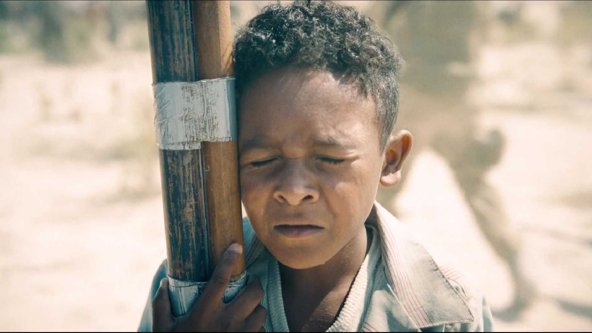 A child hugs a flagpole while calling for Superman in Superman